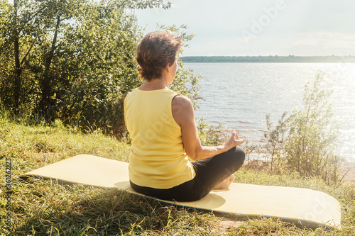 Senior woman making yoga and fitness near river in summer. Lockdown concept, sport alone. photo