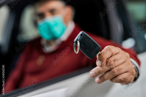 Close-up of a man with protective face mask holding new car key.