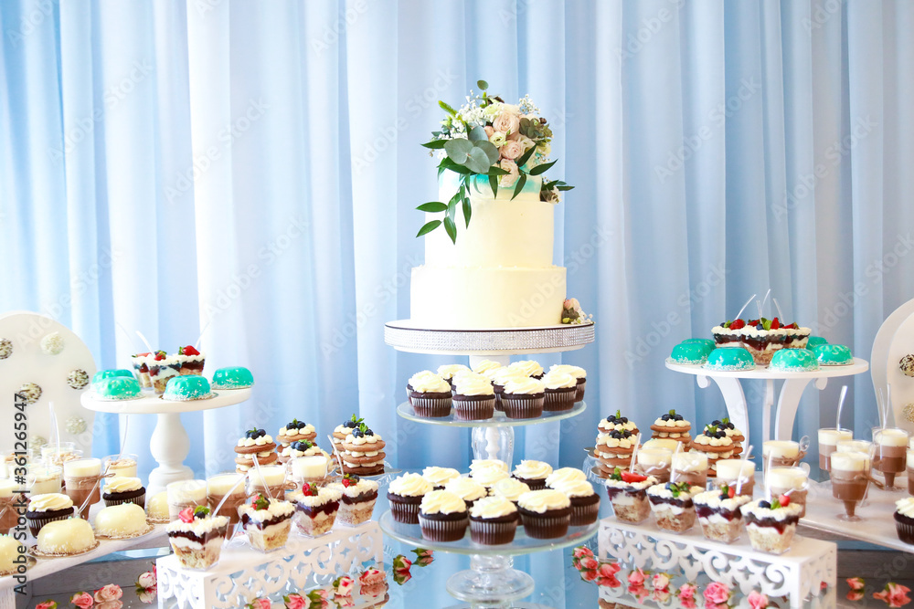 Candy bar. White wedding cake decorated by flowers standing of festive table with deserts, strawberry tartlet and cupcakes. Wedding. Reception Tartlets