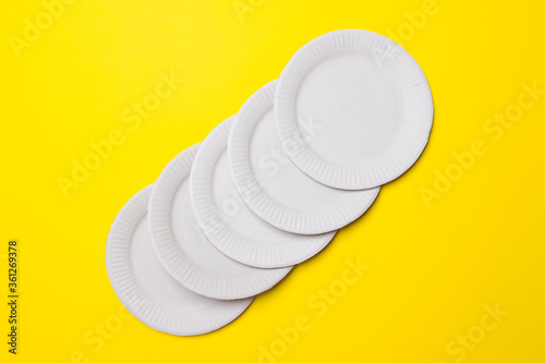 five white eco-friendly cardboard plates lie on yellow colored paper background. Top view. Close-up. Mock-up