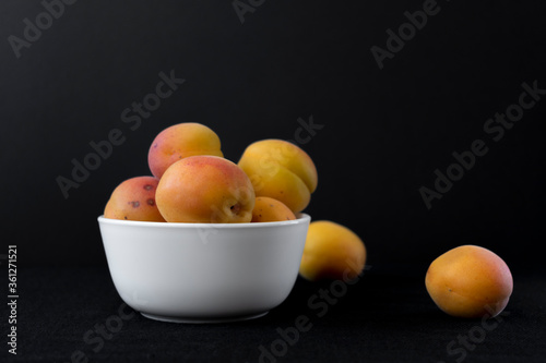 Bowl with ripe apricots on a black background