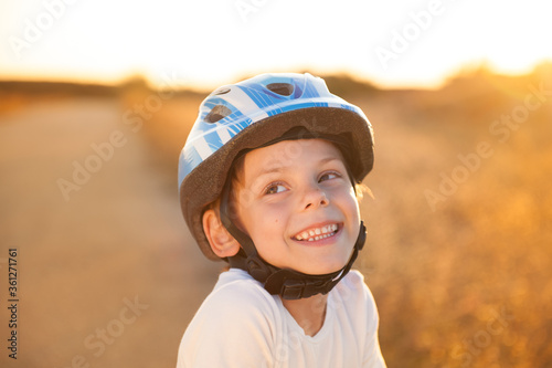 portrait of happy smiling delightful adorable little caucasian child in blue sport helmet and white shirt on summer sunset outdoors © ruslanshug