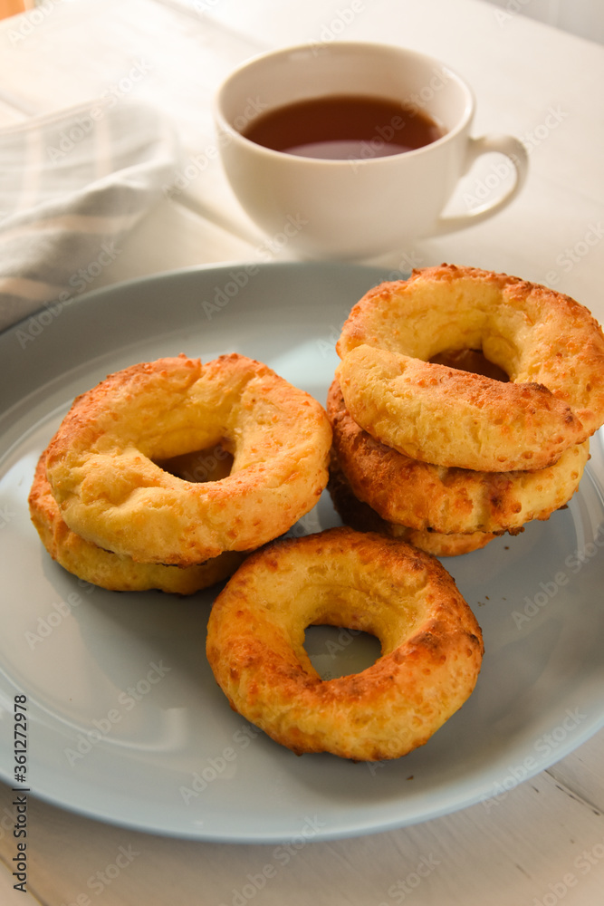 Appetizing baked bagels on a blue plate on a white wooden background with a white mug of tea and a kitchen towel Appetizing baked bagels on a blue plate on a white wooden background with a white mug of tea and a kitchen towel