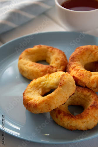 Appetizing baked bagels on a blue plate on a white wooden background with a white mug of tea and a kitchen towel