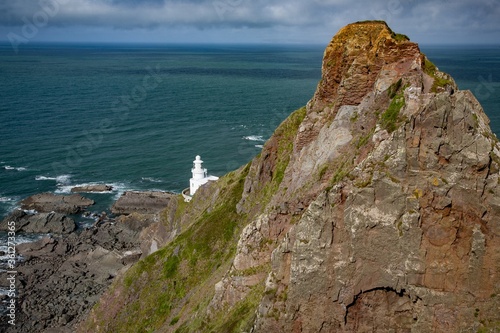 Hartland Point lighthouse surrounded by the sea and rocks under a cloudy sky in Devon, England photo