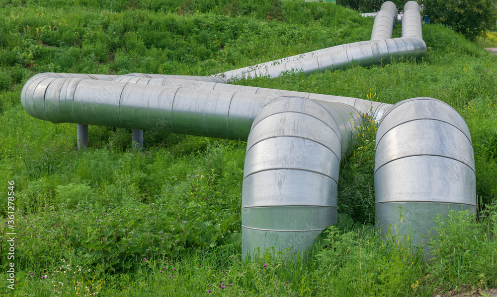 Metal pipes curving lie on a green meadow. Shiny stainless steel. Concept of gas pipeline, oil pipeline, fuel pipe, conduit, city communications. Metal pipes curving lie on a green meadow. Shiny stainless steel. Concept of gas pipeline, oil pipeline, fuel pipe, conduit, city communications.