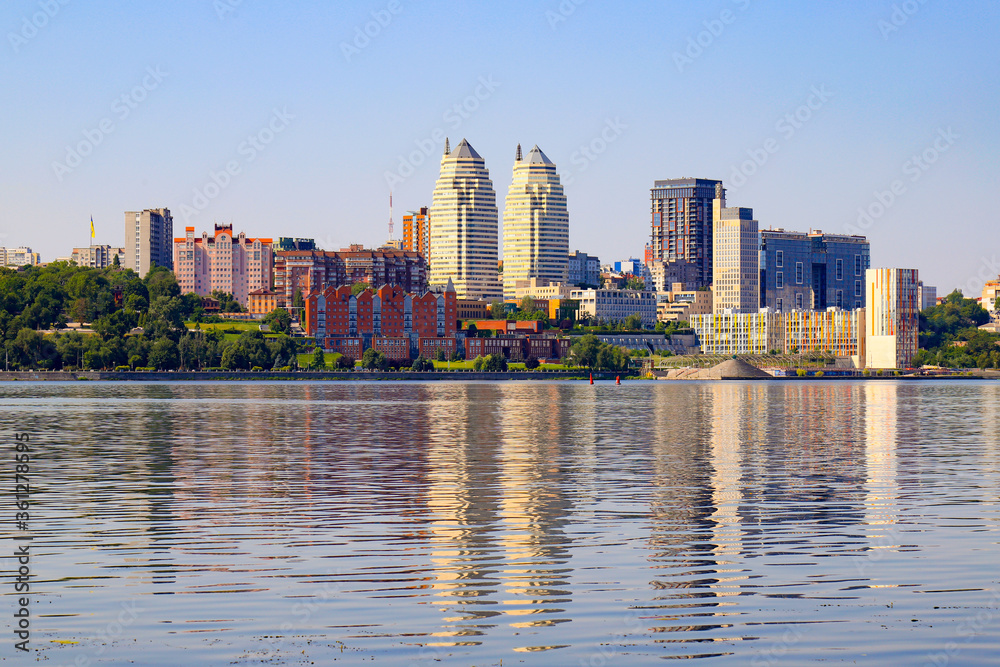 Naklejka premium Big city on the banks wide river. Beautiful modern towers, buildings, skyscrapers are reflected in the water on summer morning. Ukrainian city Dnepropetrovsk, Dnipro, Ukraine