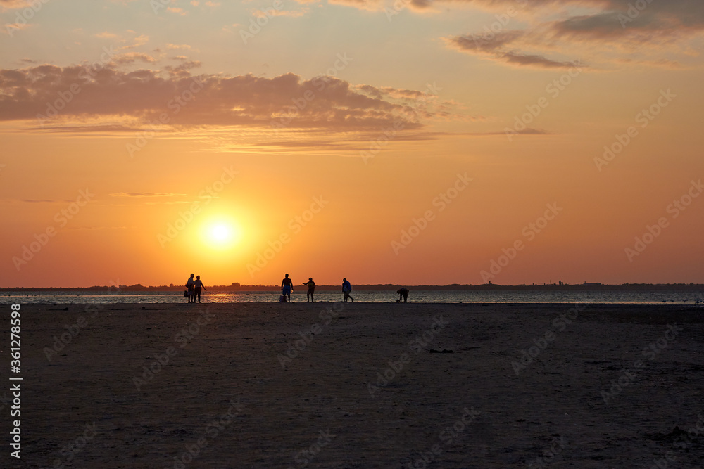 Silhouettes of people walking at sunset near the lake