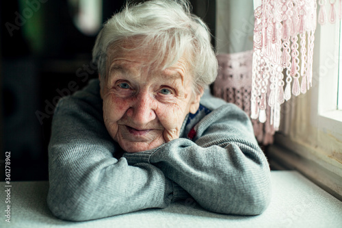 An old elderly woman, smiling portrait, looking at the camera, sitting in the kitchen.