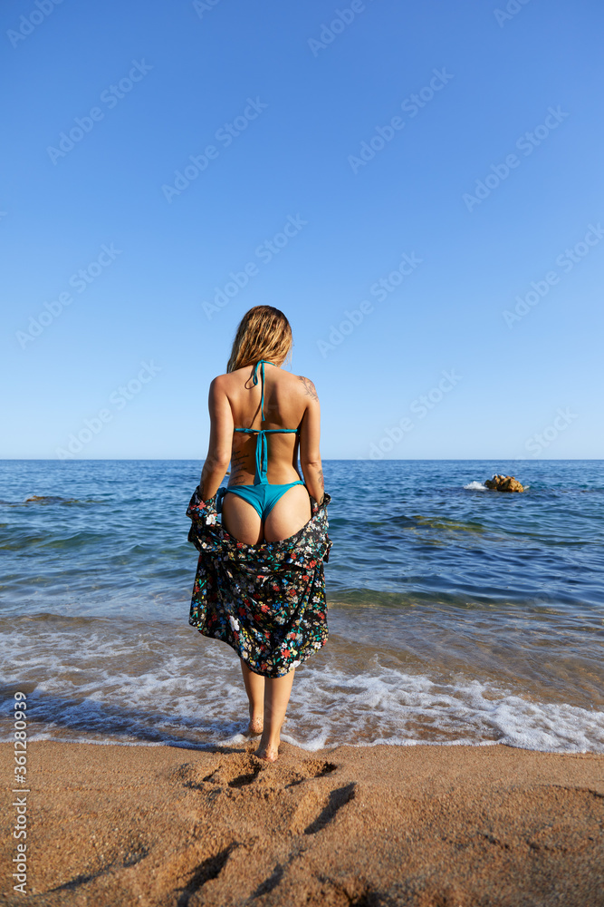 Mujer joven caminando de espaldas en la playa con bikini y camisa. Sol,  arena, verano y calor Stock Photo | Adobe Stock