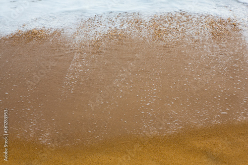 beautiful filled frame close up seascape wallpaper background shot of golden orange sand with white foamy waves of the Indian ocean forming pretty textures and patterns. Pitiwella beach, Sri Lanka