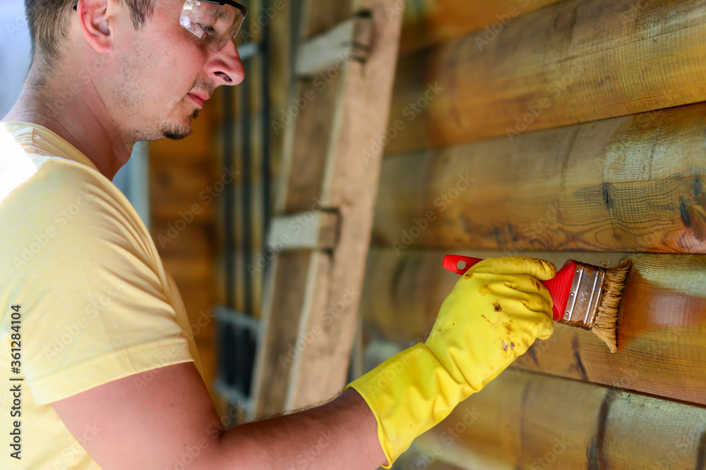 Painter holding a paintbrush over wooden surface, protecting wood for exterior influences and weathering. Carpentry, wood treatment, hard at work, home improvement, do-it-yourself concept. Painter holding a paintbrush over wooden surface, protecting wood for exterior influences and weathering. Carpentry, wood treatment, hard at work, home improvement, do-it-yourself concept.