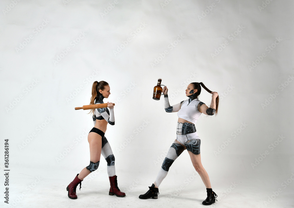 beautiful girls in costumes of robots quarreled and fight with a rolling pin and a big bottle