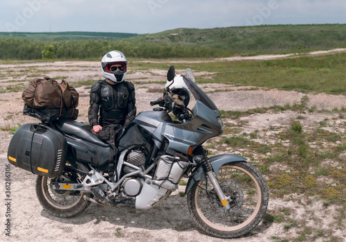 Girl motorcyclist in a helmet. Dressed in a jacket with a turtle  body armor  knee pads. Traveling is an extreme hobby. Safety and body protection. Bike with bags. Copy space panorama.
