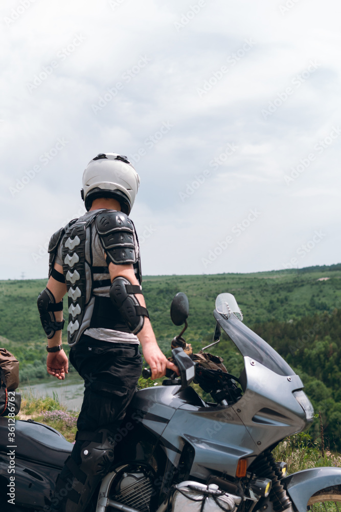 Biker in a helmet and motorcycle equipment, jacket turtle, body armor. Close. In the background a touristic motorcycle. The concept of extreme and hobby. Traveling by bike. vertical photo