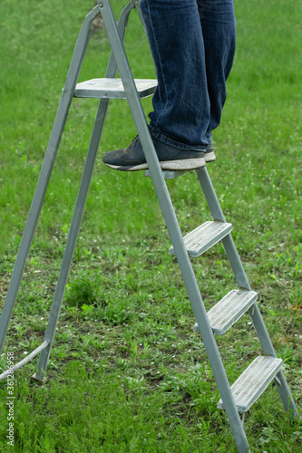 Male feet standing on metal ladder step in garden on green grass lawn. Man working in the garden. Personal growth, career development, progress, goals concept