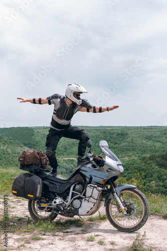 Extreme stunt on a bike. Like surfing. Motorcycle driver wearing a turtle jacket, body armor and a helmet. Stands on top. Vertical photo. The concept of freedom of new impressions and tourism.