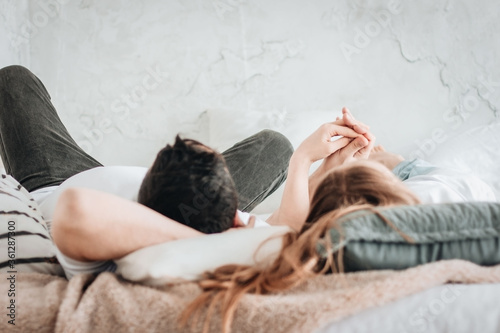 Young straight couple laying on backs on bed holding hands. side view 