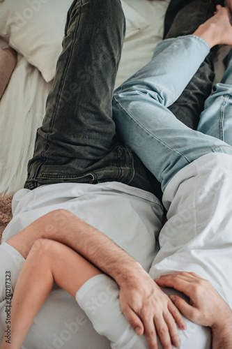 Couple in jeans and white t shirts lying in bed on sheets hugging, cuddling, caressing. Love, relationship concept