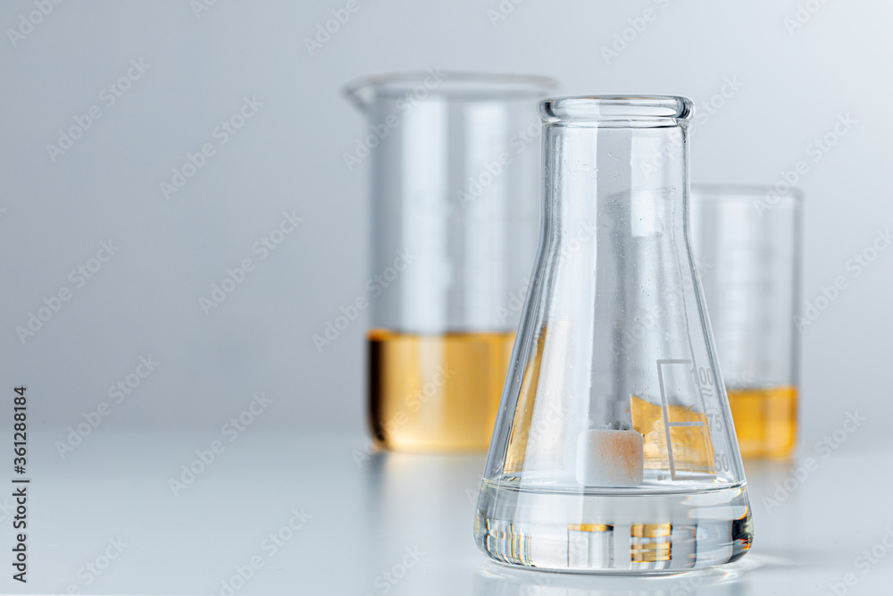 Laboratory glassware with yellow oily liquid on grey background Laboratory glassware with yellow oily liquid on grey background