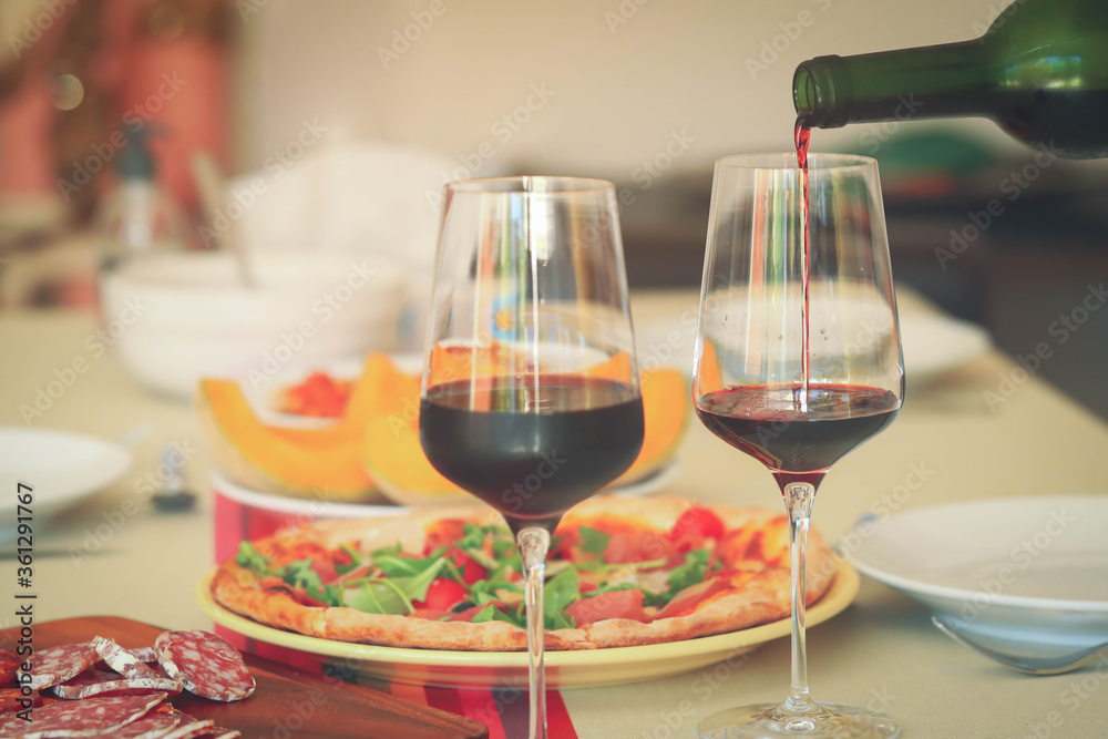 Pouring red wine from bottle into glasses on table with food background Pouring red wine from bottle into glasses on table with food background