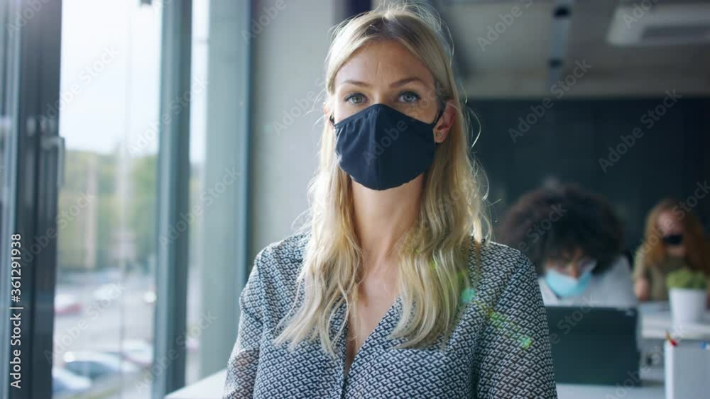 Young woman back at work in office after lockdown, taking off face mask.