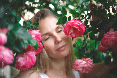 blond woman smiling in a flowering bush of pink roses