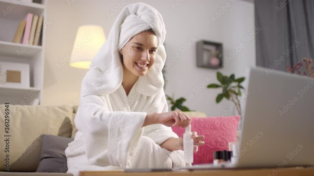 Modern young woman sitting on sofa in living room after taking morning shower removing nail polish and talking with someone on web camera Modern young woman sitting on sofa in living room after taking morning shower removing nail polish and talking with someone on web camera