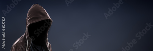 Invisible man wearing a hoodie on dark panoramic background with copy space, dealer or burglar header