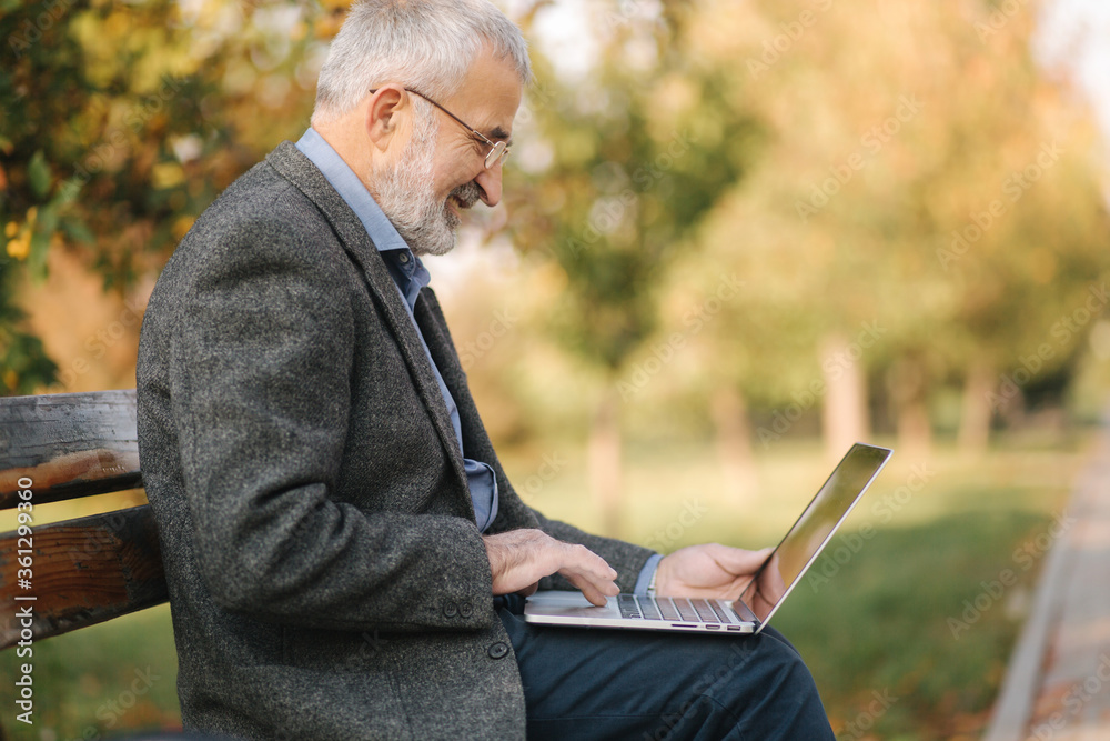 Elderly man use laptop in the park. Handsome senior man in glasses work outside Elderly man use laptop in the park. Handsome senior man in glasses work outside