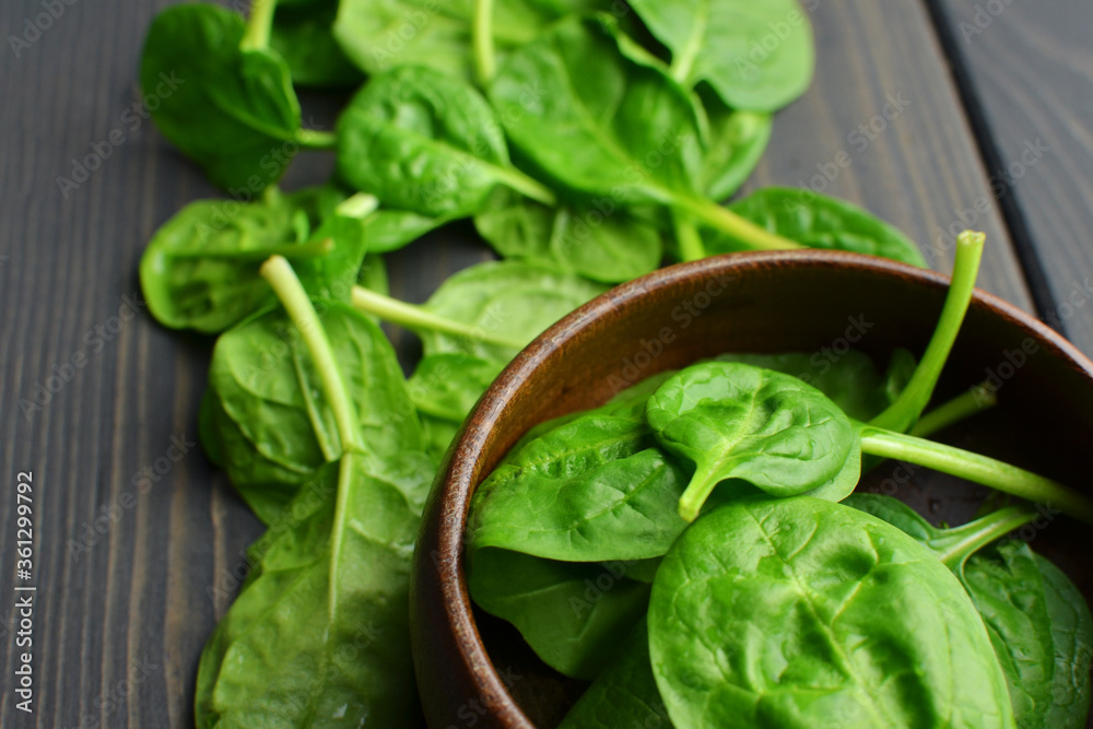 Fresh spinach leaves in wooden bowl over old wooden table. Healthy vegan food. Green living and eco-conscious concept. Fresh spinach leaves in wooden bowl over old wooden table. Healthy vegan food. Green living and eco-conscious concept.