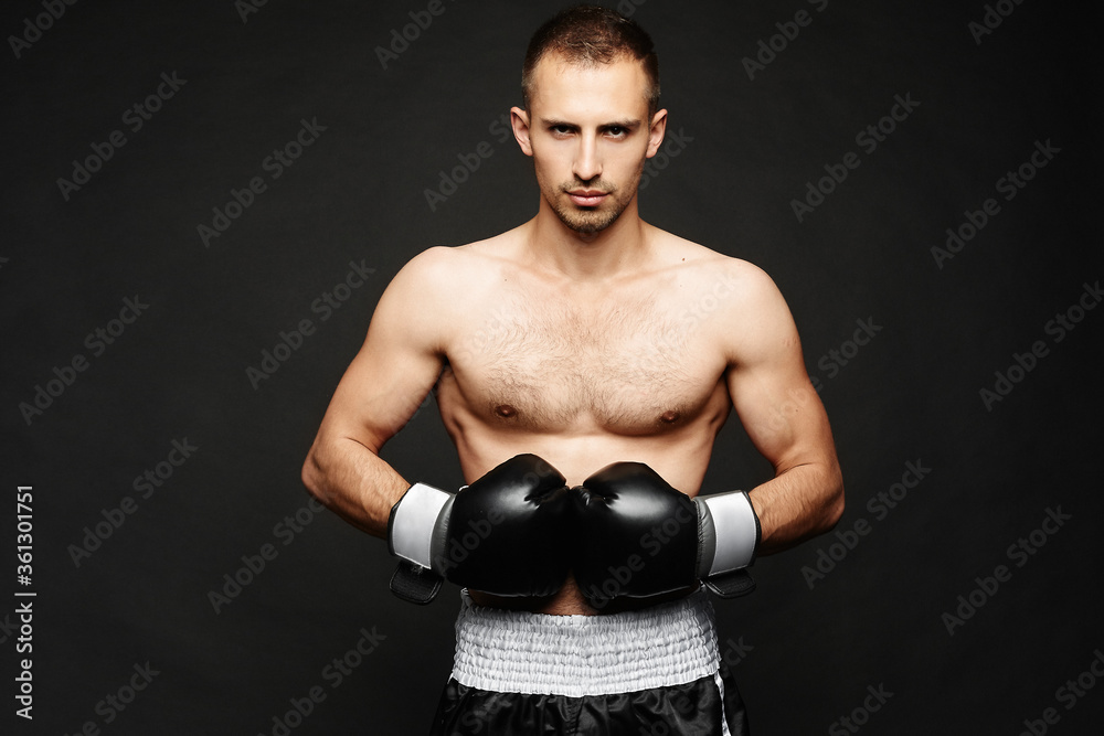 A young male boxer with athletic perfect body in boxing gloves isolated at dark background