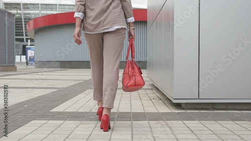 Business female legs in red shoes with high heels. Successful business girl goes towards the business center.