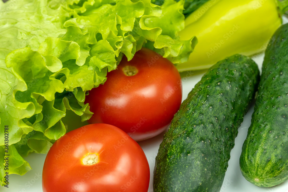 beautiful fresh, juicy vegetables on a white plate: fresh peppers, tomatoes, cucumbers, lettuce, dill