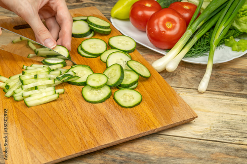 women's hands with a knife cut a cucumber on a cutting Board, next to a plate of vegetables