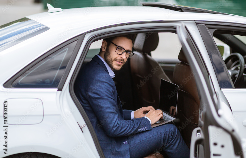 Handsome businessman working with laptop computer sitting at back seat of car, empty space for design on screen Handsome businessman working with laptop computer sitting at back seat of car, empty space for design on screen