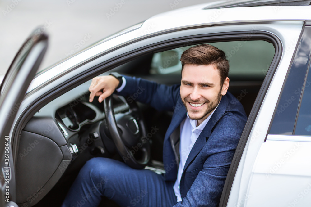 Portrait of smiling corporate employee sitting on driver's seat of his auto