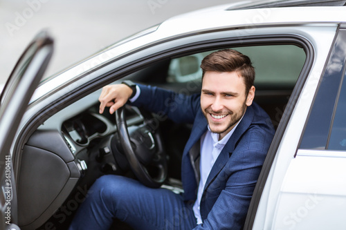 Portrait of smiling corporate employee sitting on driver's seat of his auto