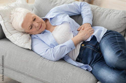 Acute Pancreatitis. Sad elderly woman holding her abdomen  suffering from stomach ache