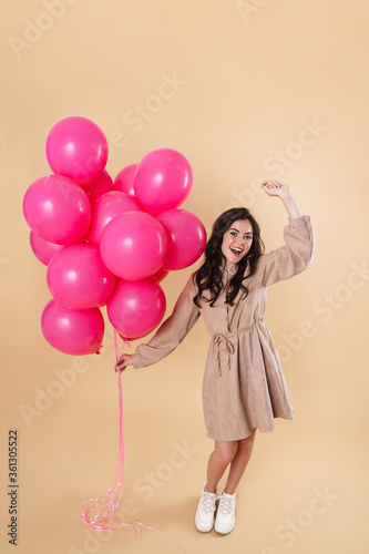 Image of excited cute woman laughing and dancing with pink balloons