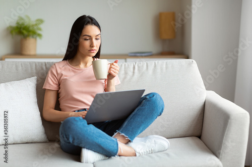 Girl Using Laptop Having Coffee Sitting On Couch At Home