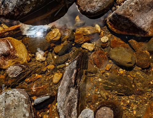 Brown and red pebbles and stones in crystal water with a reflection of sun