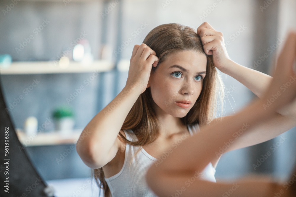 Millennial woman with problematic hair looking in mirror at bathroom, blank space Millennial woman with problematic hair looking in mirror at bathroom, blank space