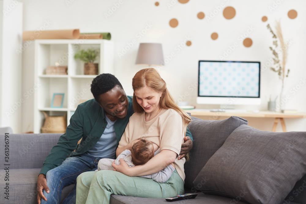 Portrait of happy interracial family sitting on couch at home together with  mature mother breastfeeding baby, copy space foto de Stock | Adobe Stock