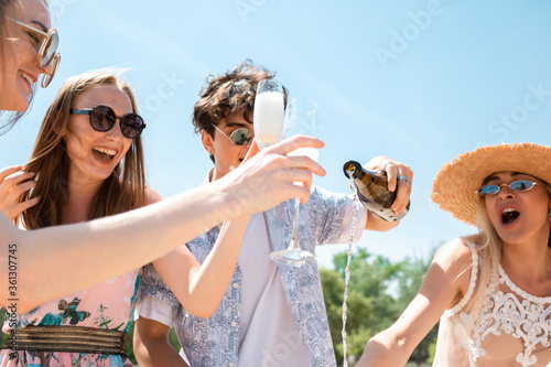 Pouring champagne, clinking glasses. Seasonal feast at beach resort. Group of friends celebrating, resting, having fun in sunny summer day. Look happy and cheerful. Festive time, wellness, holiday