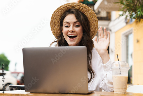 Portrait of woman waving hand while making video call on laptop in cafe