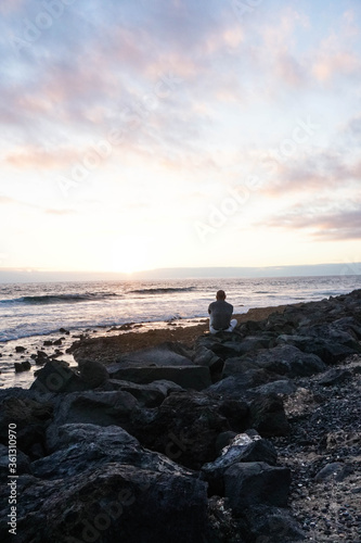 Old man on the rocks looking at the sea at sunset