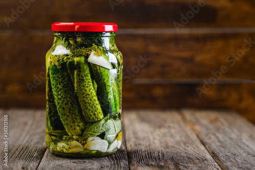 Pickled cucumbers in a jar on a wooden background, harvesting seasonal vegetables