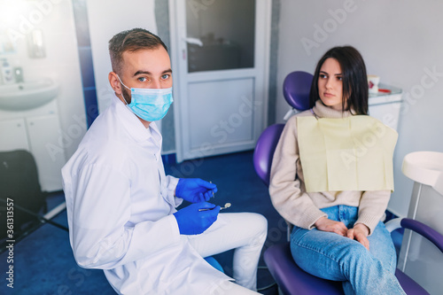 dentist in uniform holds dental tools and looks into the camera. © Ivan