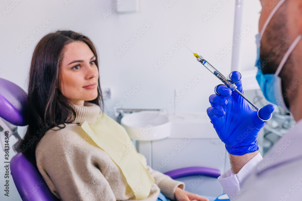 Dentist's hands with blue gloves holding a syringe. Patient in d Dentist's hands with blue gloves holding a syringe. Patient in d